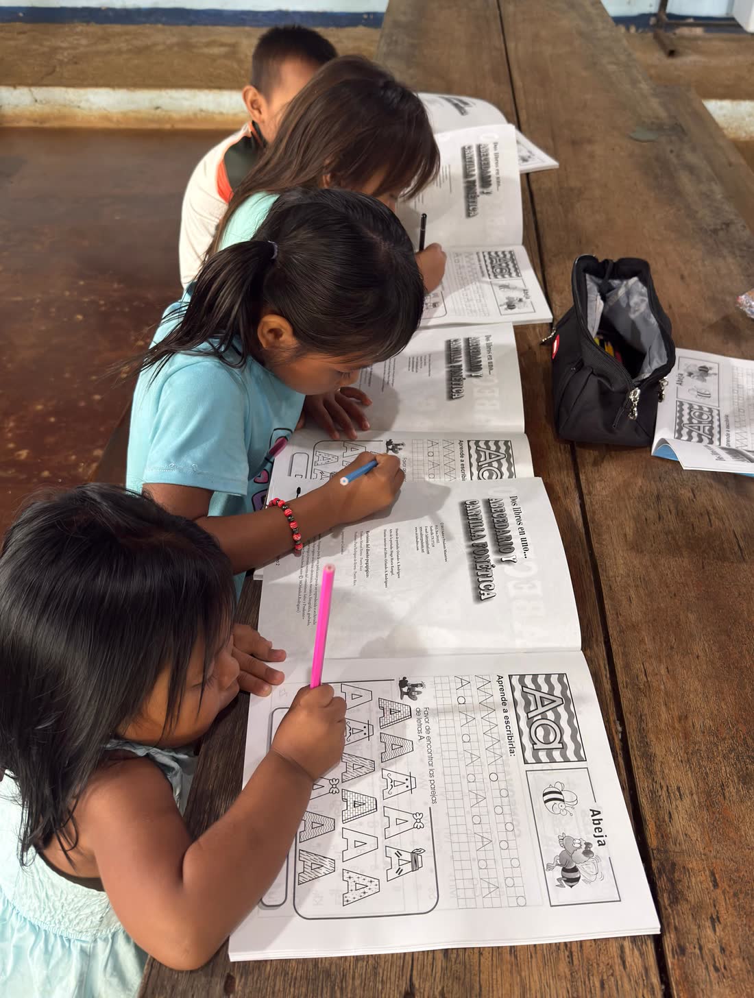 Tres niñas escribiendo las primeras letras en la cartilla fonética