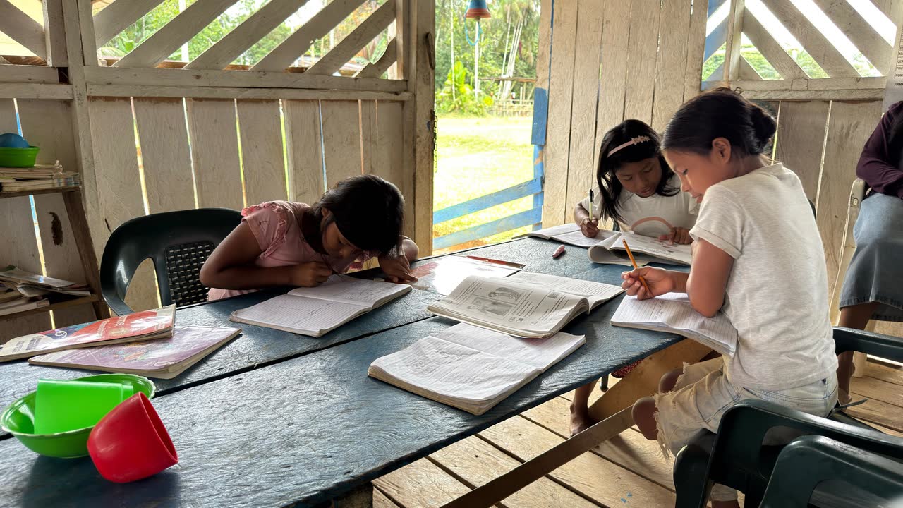 Tres niñas escribiendo en sus cuadernos alrededor de una mesa de madera