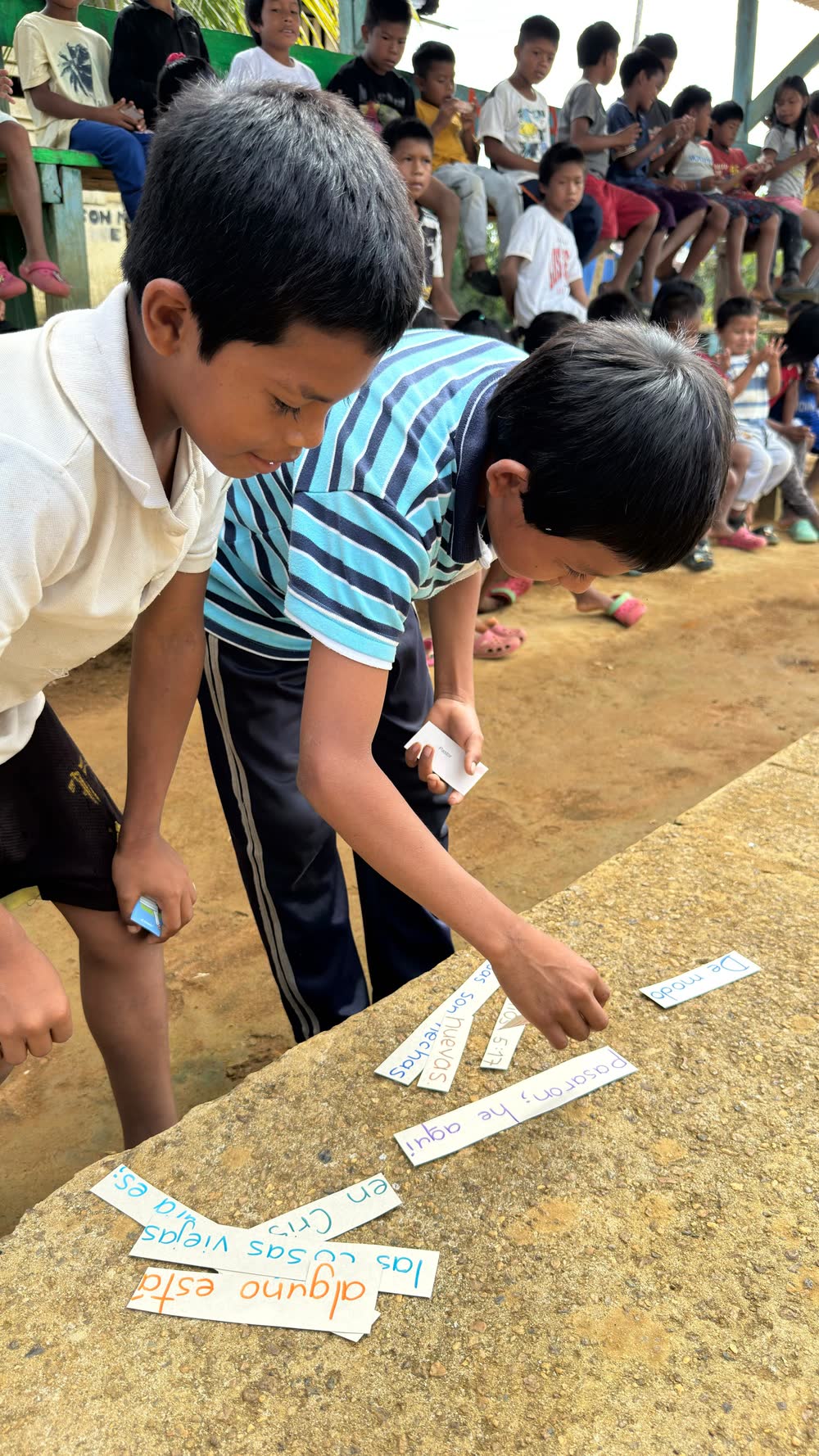Dos niños ordenando tarjetas con palabras sobre el piso de cemento